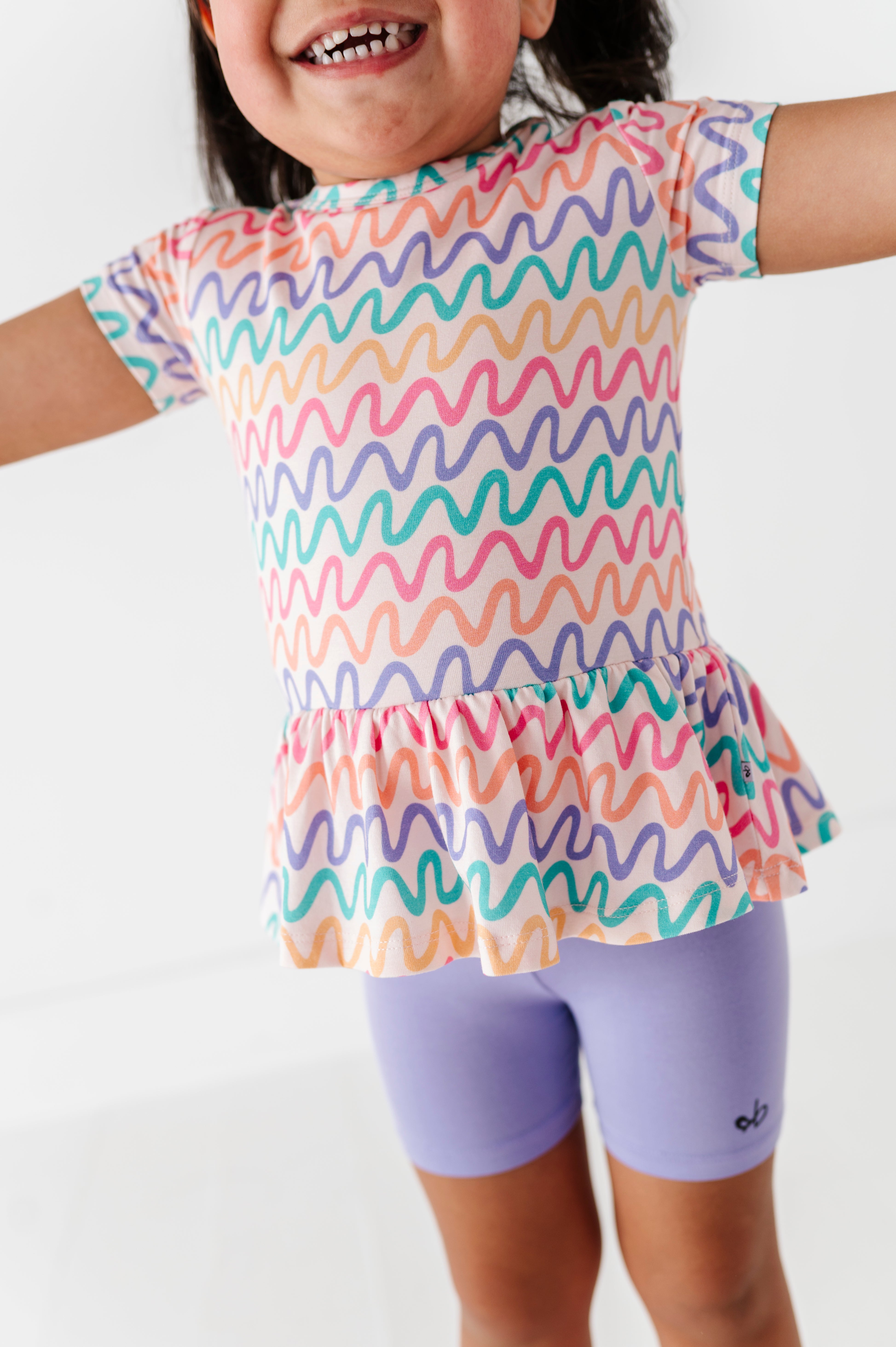 Child wearing a colorful wavy patterned top and purple biker shorts on a white background