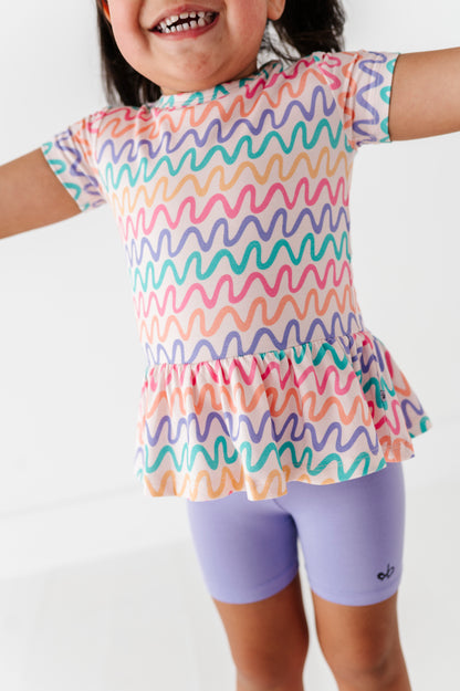 Child wearing a colorful wavy patterned top and purple biker shorts on a white background