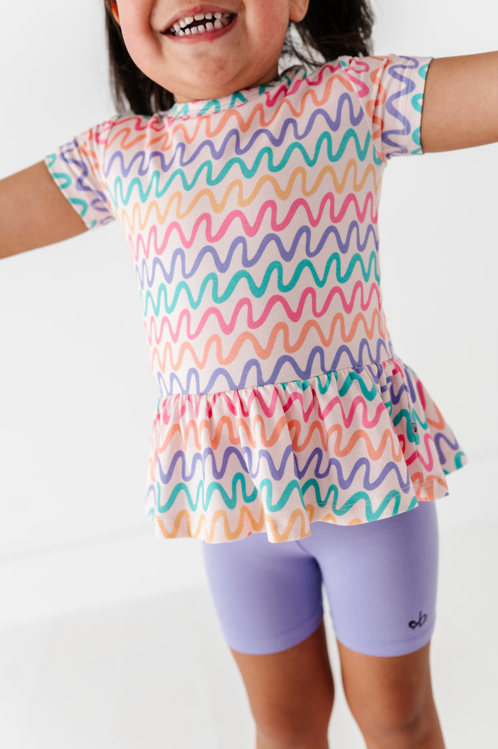 Child wearing a colorful wavy patterned top and purple biker shorts on a white background