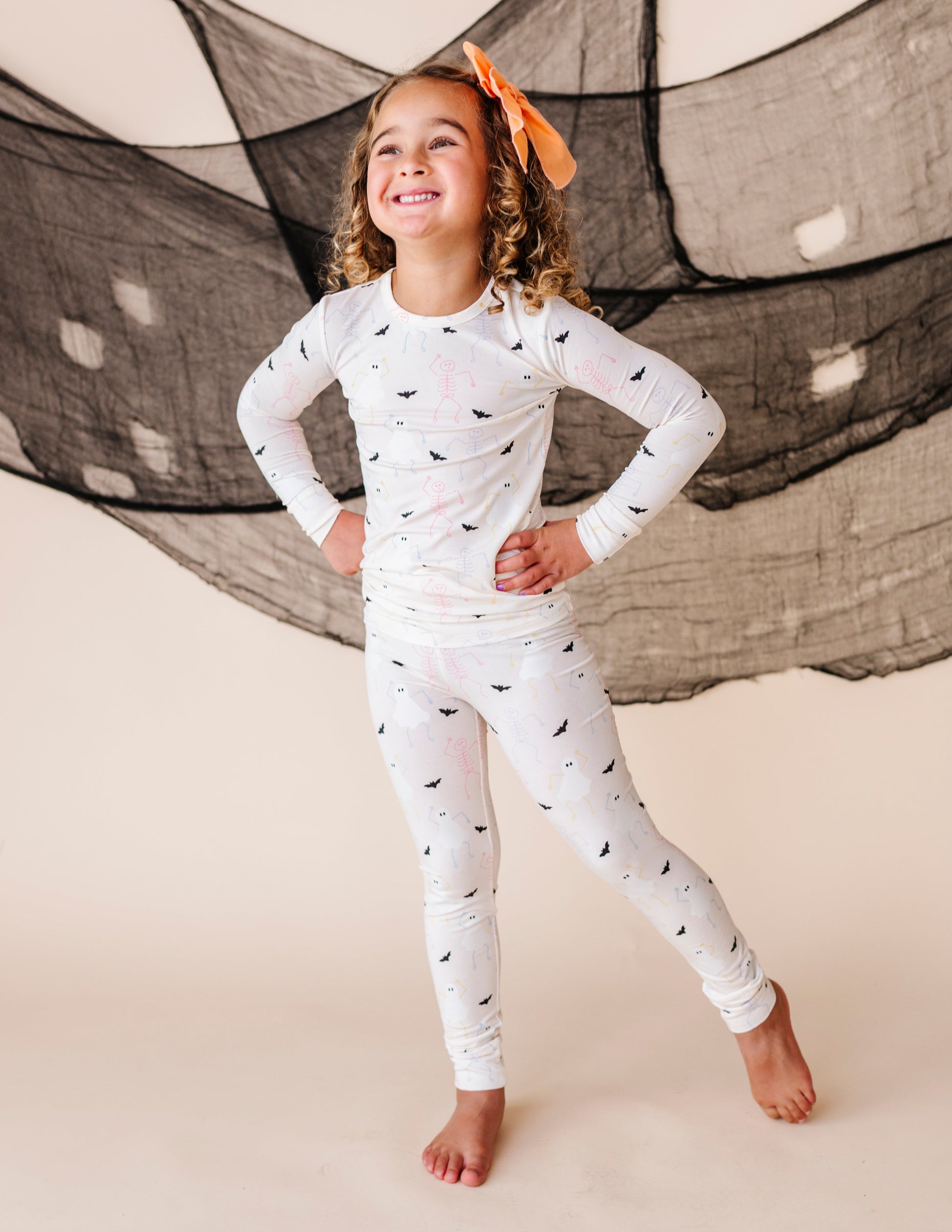 Child wearing a cream pajama set with halloween  patterns in front of a large net.
