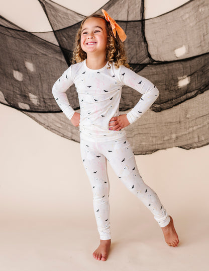 Child wearing a cream pajama set with halloween  patterns in front of a large net.