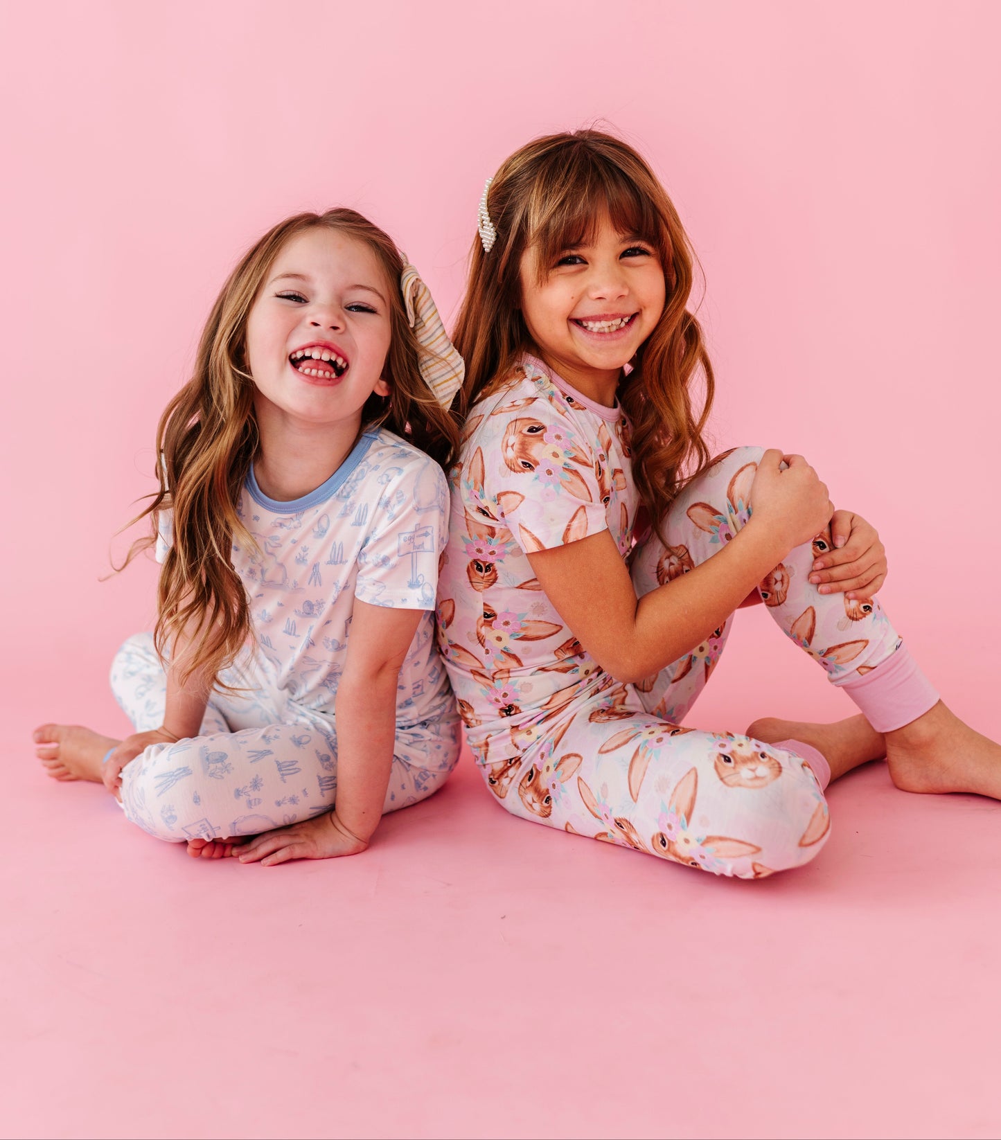 Two children in matching Easter pajamas sitting on a pink background