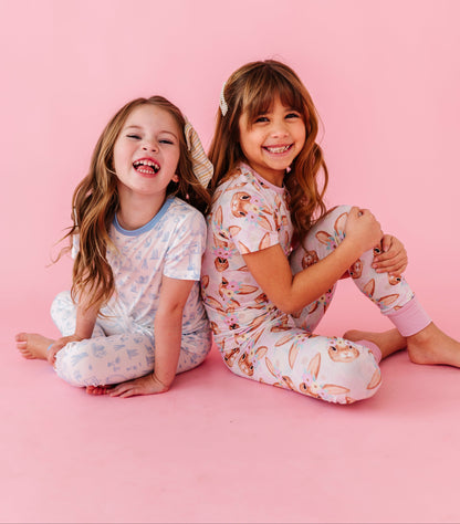 Two children in matching Easter pajamas sitting on a pink background