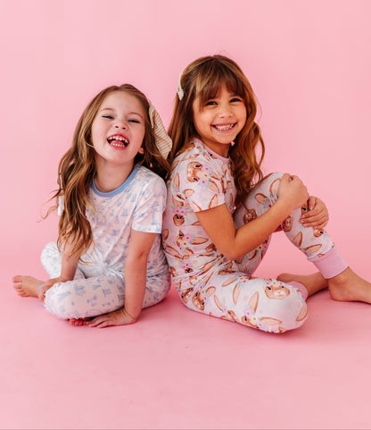 Two children in matching bamboo pajamas sitting on a pink background