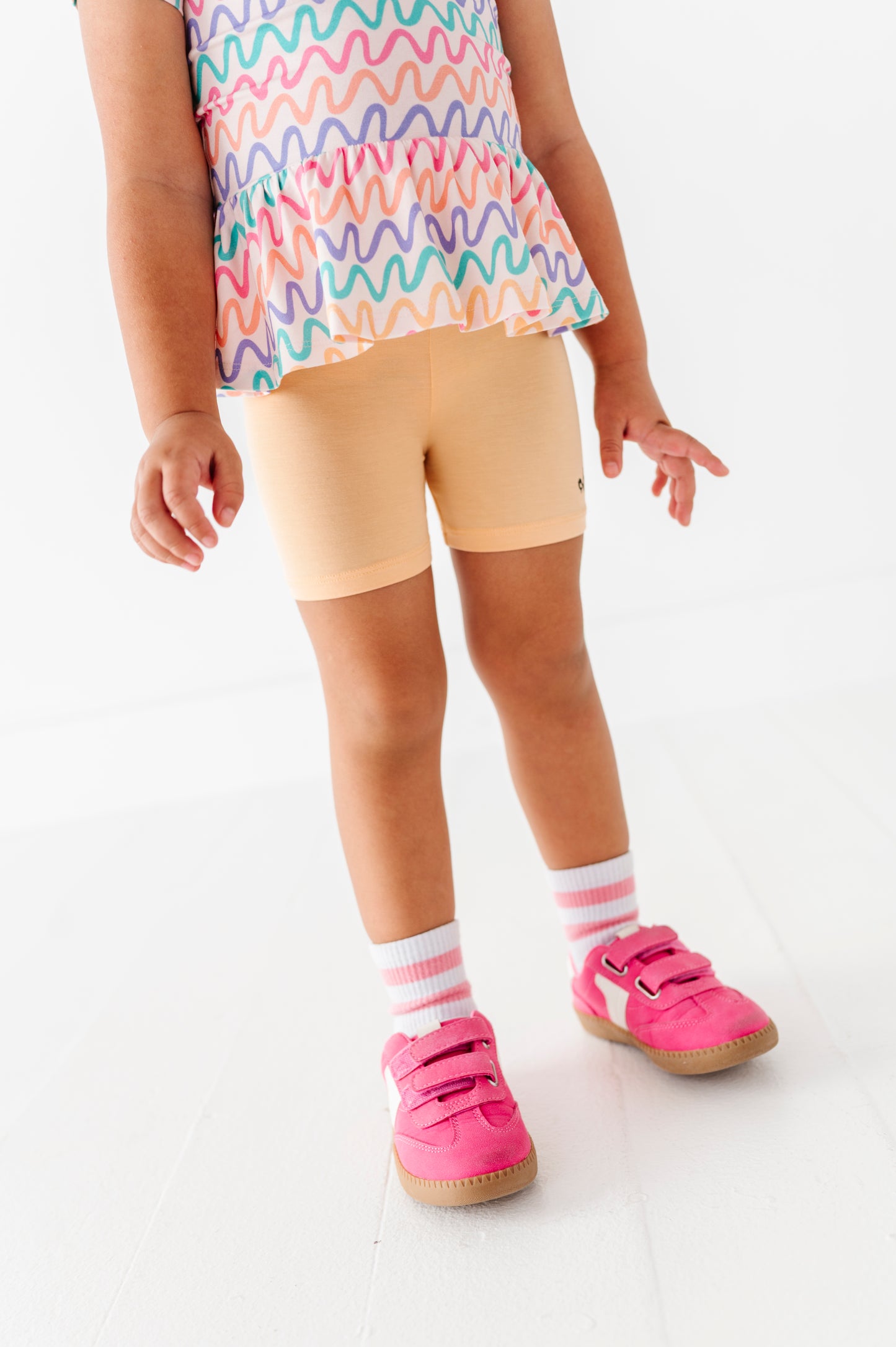 Child wearing a colorful top, yellow bamboo biker shorts, pink shoes, and striped socks on a white background