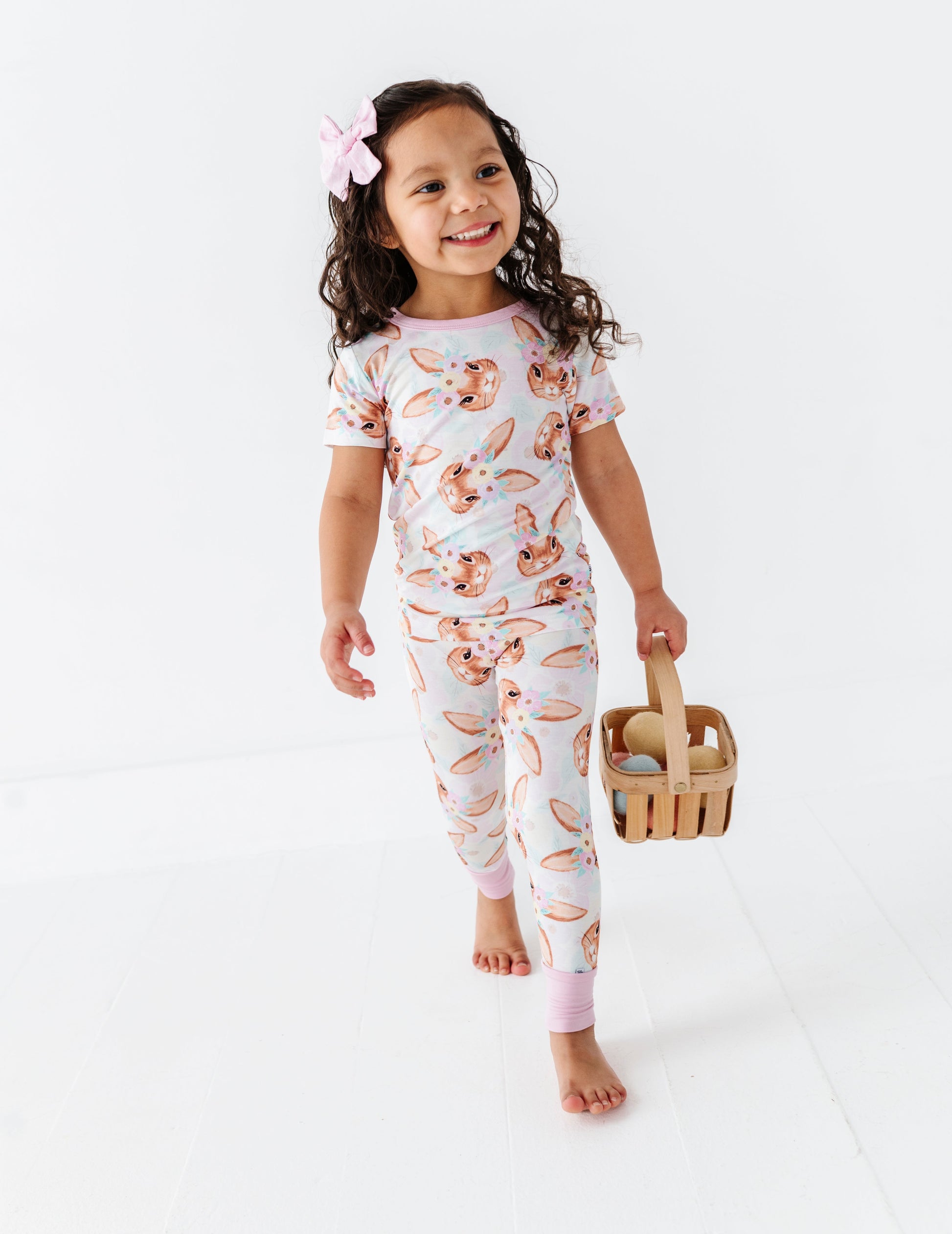 Child wearing a floral bamboo two-piece set holding an Easter basket on a white background