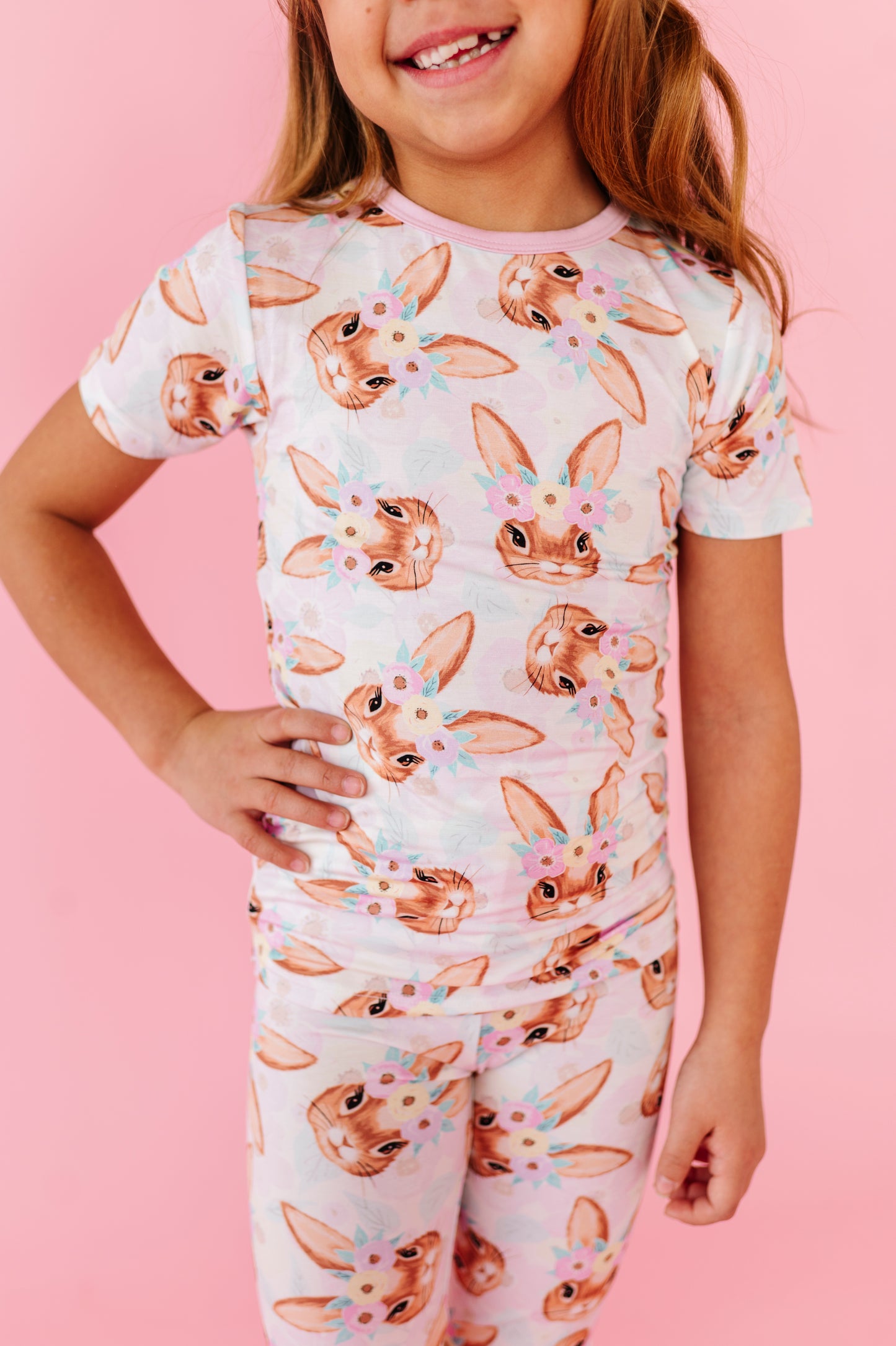 Child wearing an Easter pajama set with bunny print on a pink background