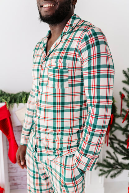 A side view of a man wearing a bamboo lounge set in a classic Christmas plaid print, standing in front of a fireplace and a Christmas tree