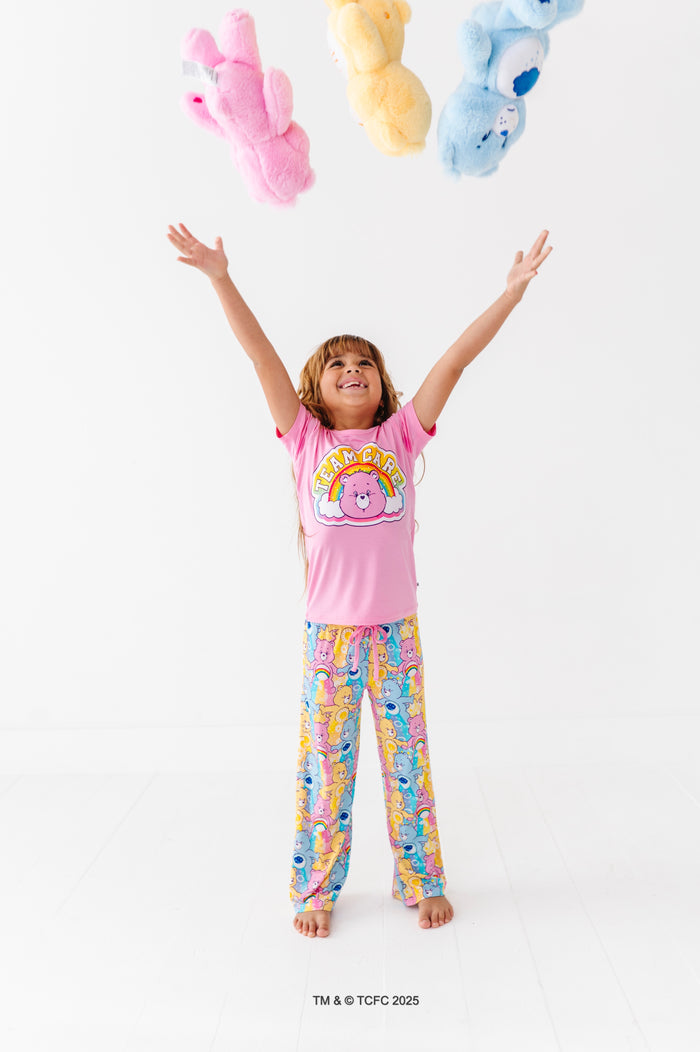Kid in Care Bears™ Stare bamboo pajama set tossing plush Care Bears toys in the air