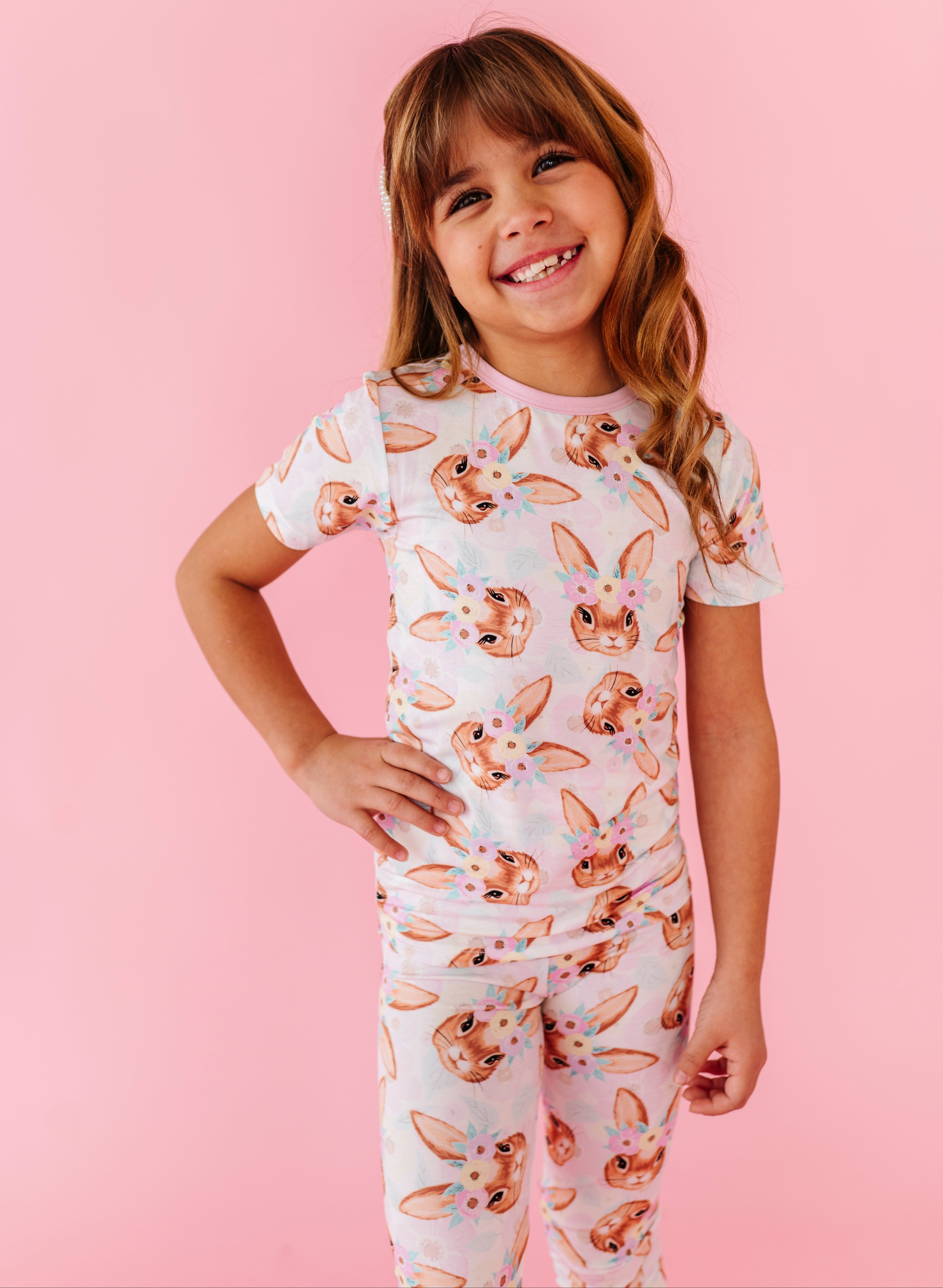 Young girl wearing an Easter bamboo pajama set with animal print on a pink background