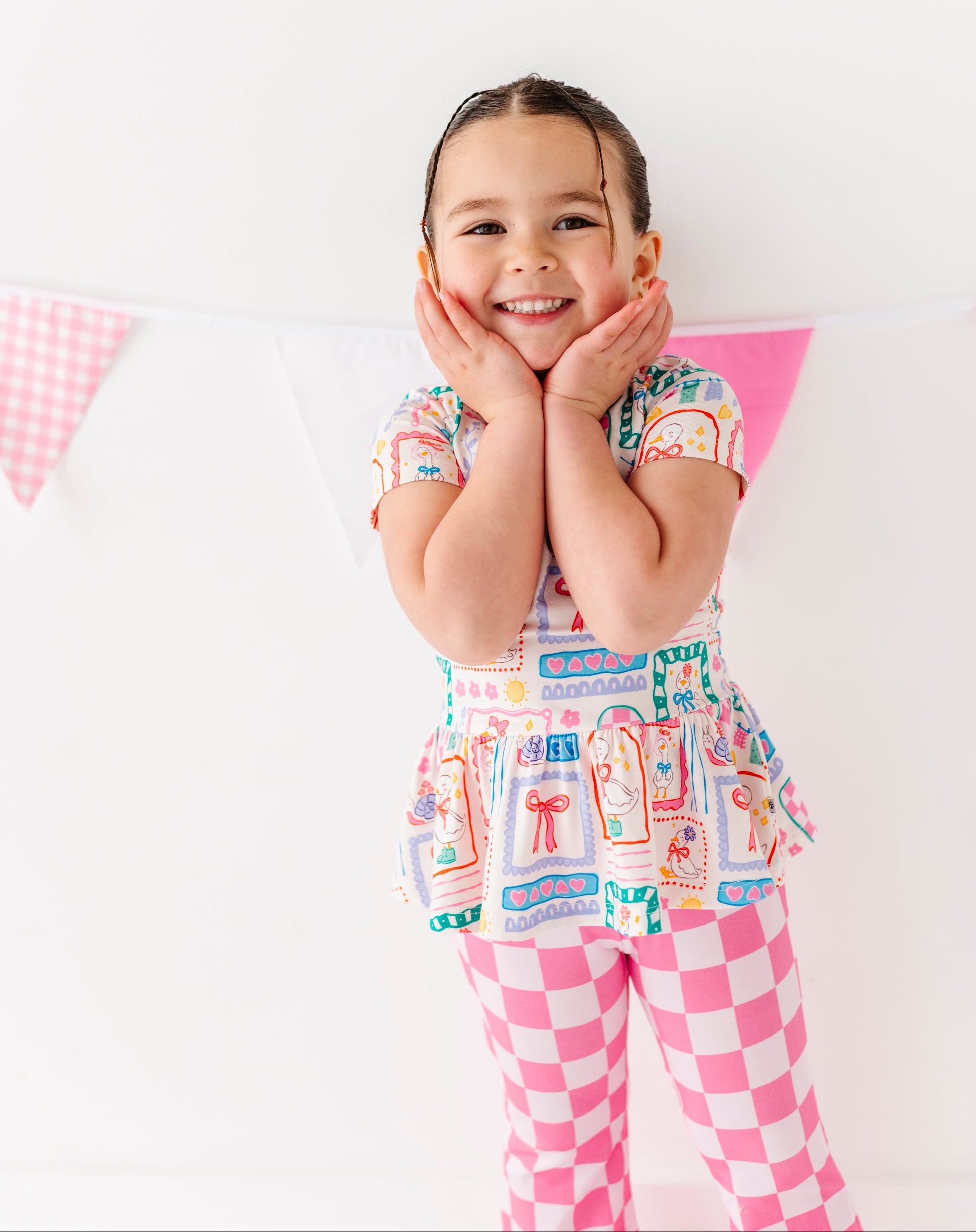 Child wearing a colorful bamboo/cotton blend peplum top with a checkered pattern pants on a white background