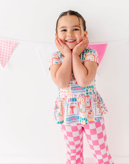 Child wearing a colorful bamboo/cotton blend peplum top with a checkered pattern pants on a white background