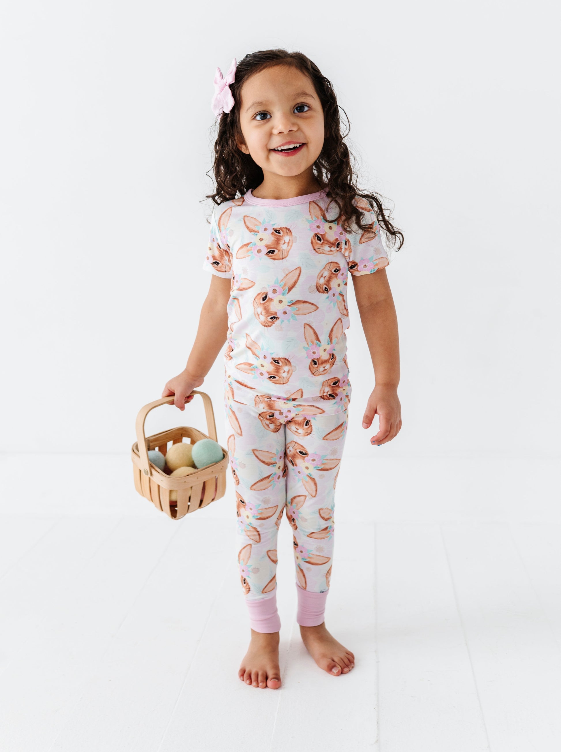 Child wearing a pajama set with bunny print holding a basket of Easter eggs on a white background