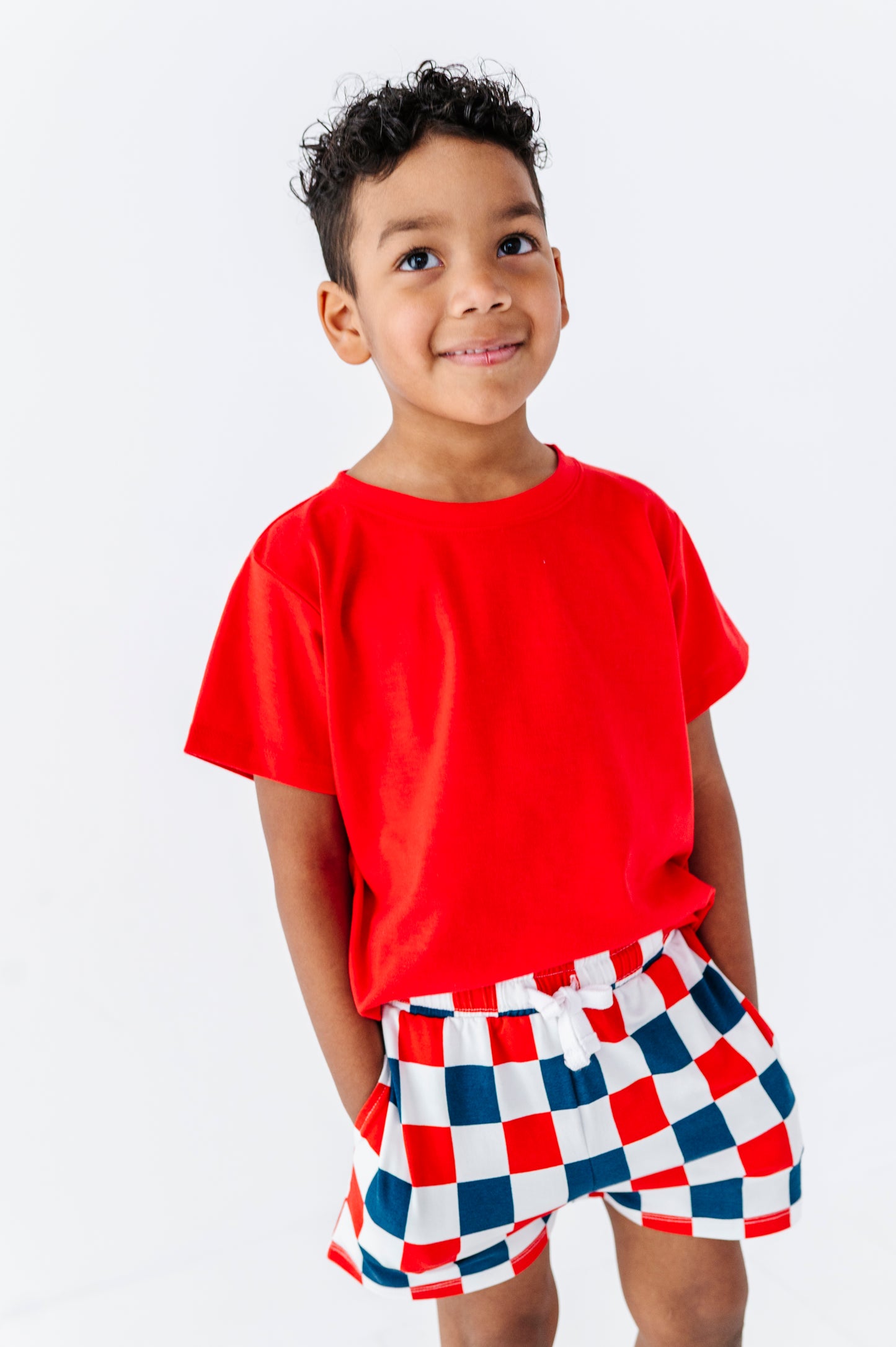 Child wearing a red shirt and checkered shorts on a white background