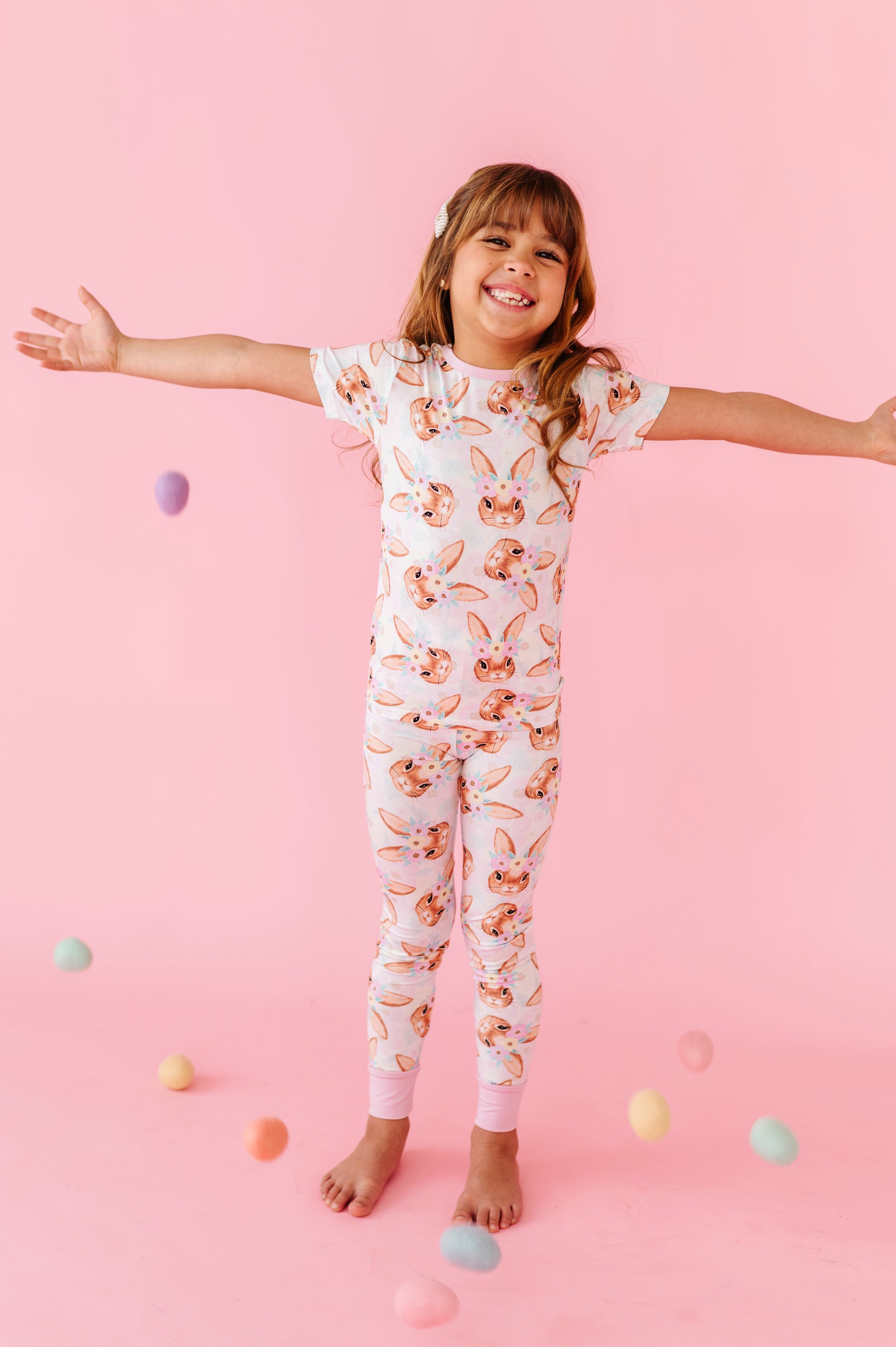 Child wearing a floral bamboo Easter onesie on a pink background with colorful eggs scattered around