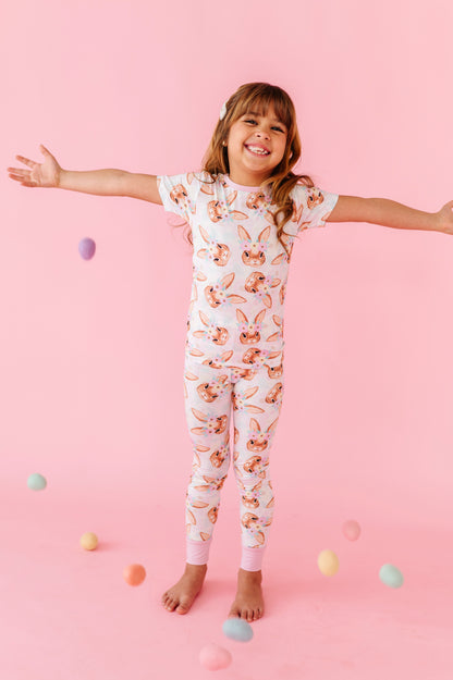 Child wearing a floral bamboo Easter onesie on a pink background with colorful eggs scattered around