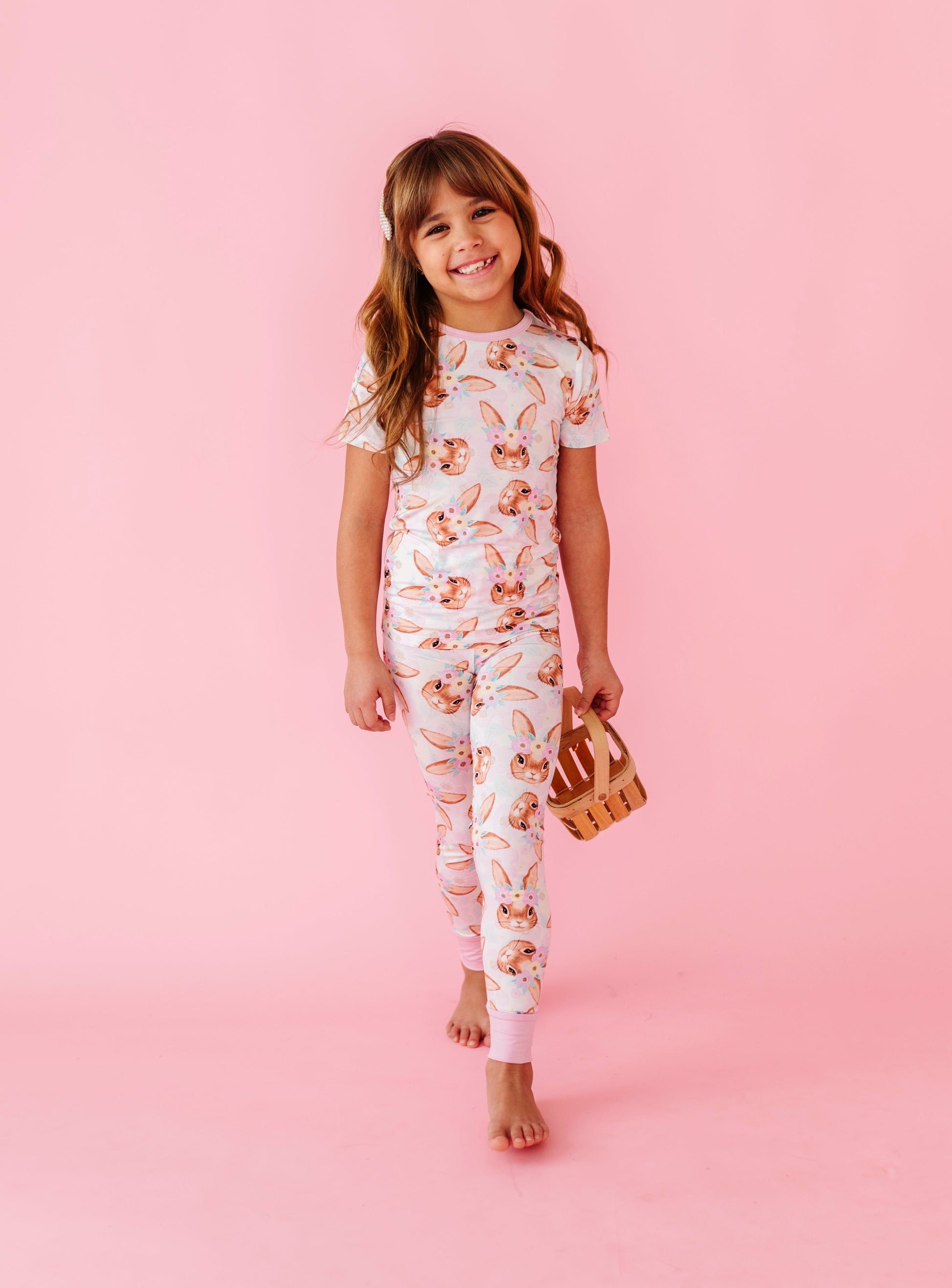 Young girl wearing a floral and bunny bamboo pajama set on a pink background