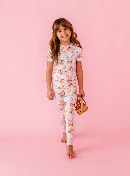Young girl wearing a floral and bunny bamboo pajama set on a pink background