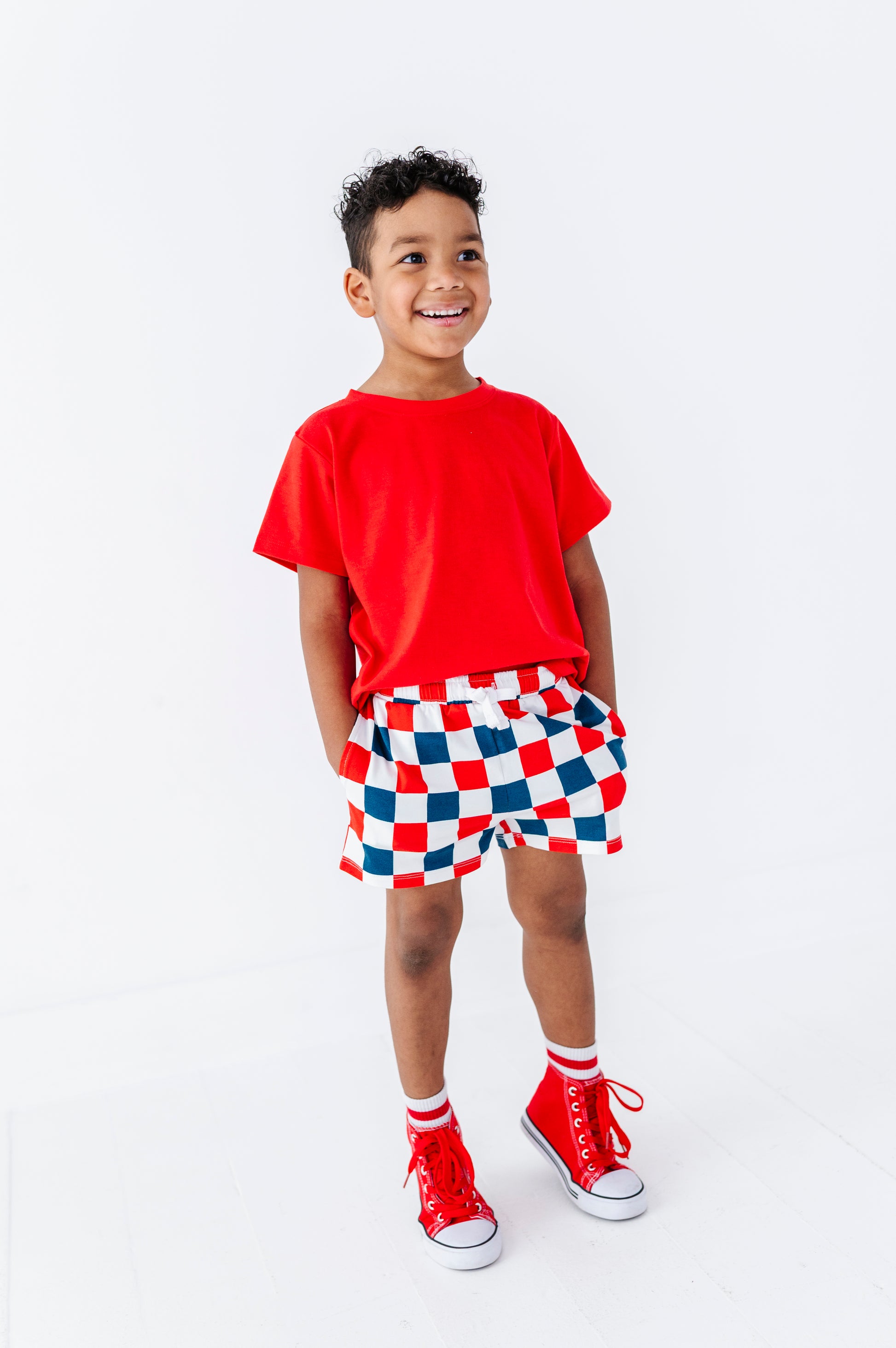 Child wearing a red shirt and checkered shorts on a white background