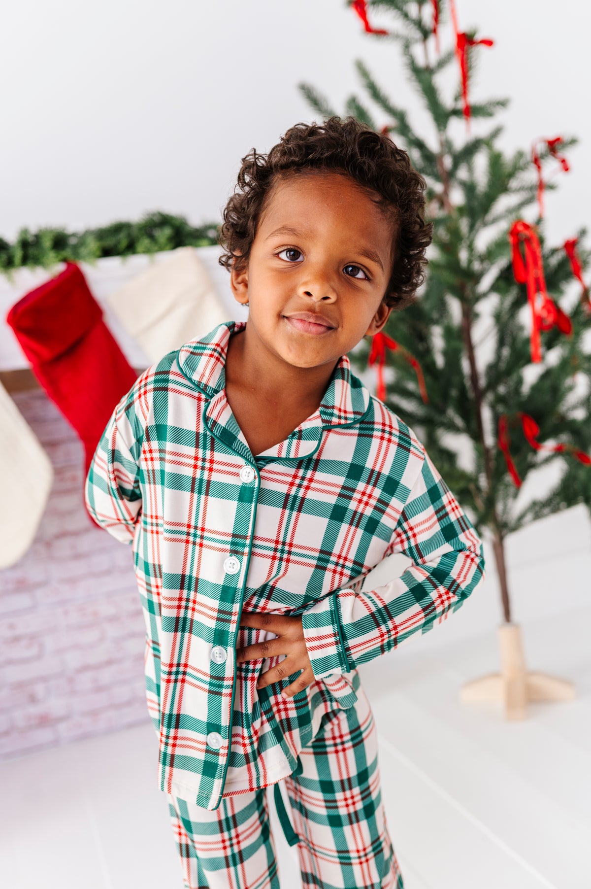 A little boy wearing classic Christmas pajamas in a red, green, and cream print 