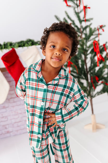 A little boy wearing classic Christmas pajamas in a red, green, and cream print 