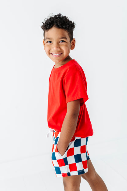 Child wearing a red shirt and checkered shorts on a white background