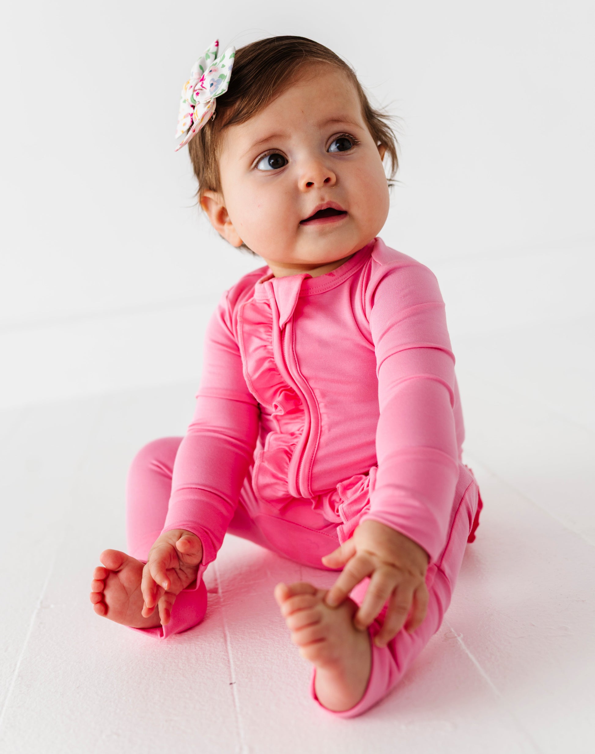 Baby in a pink bamboo zip romper sitting on a white surface