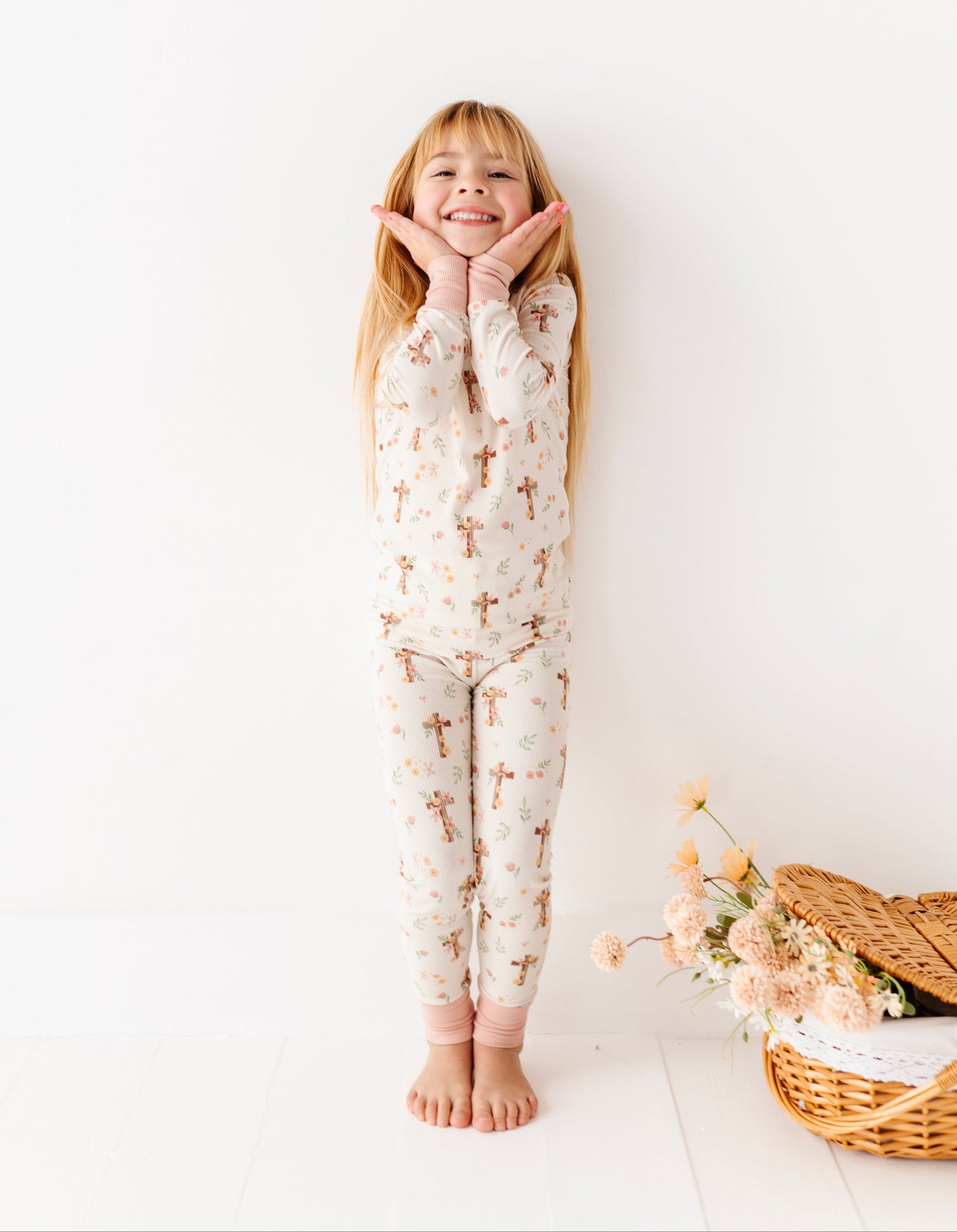 Child wearing a floral bamboo pajama set standing against a white wall with a basket of flowers on the floor.
