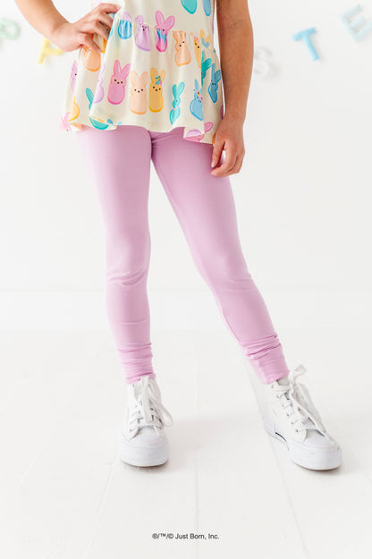Child wearing a colorful top with PEEPS® and purple  leggings on a white background