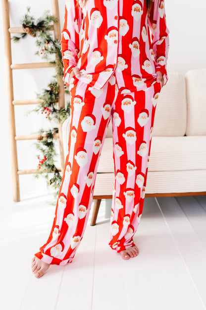 A person wearing a red and white Santa Claus patterned bamboo pajama set, standing barefoot in a bright room with a sofa and holiday ladder visible in the background.