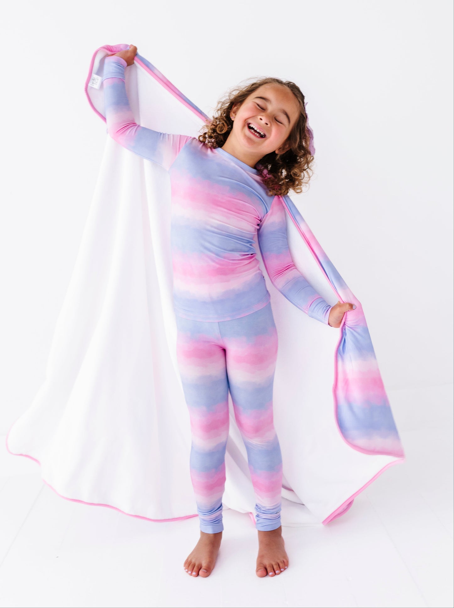 Child wearing a pink and blue tie-dye bamboo pajama set with a matching bamboo blanket on a white background