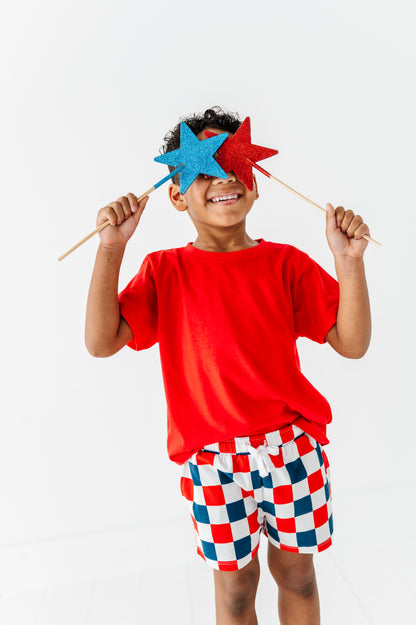 Child wearing a red shirt and checkered shorts holding red and blue star-shaped objects against a white background