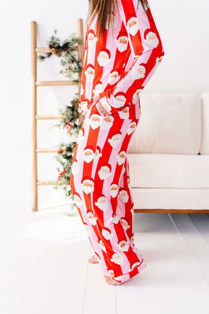 A person wearing a red and white Santa Claus patterned bamboo pajama set, standing in a bright room with a white sofa and a wooden ladder decorated with greenery.