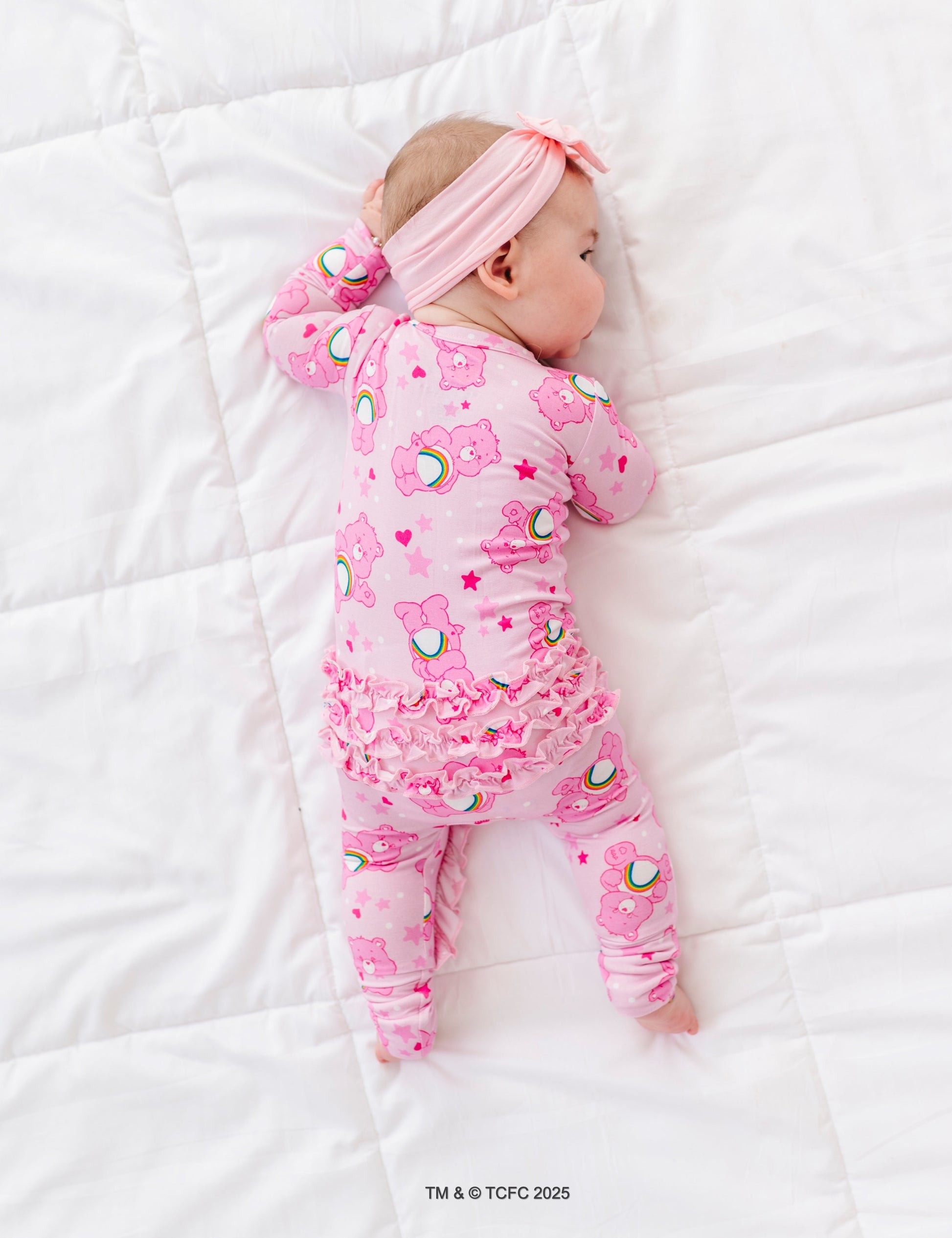 Baby resting on white bedding in Care Bears Cheer Bear bamboo sleeper