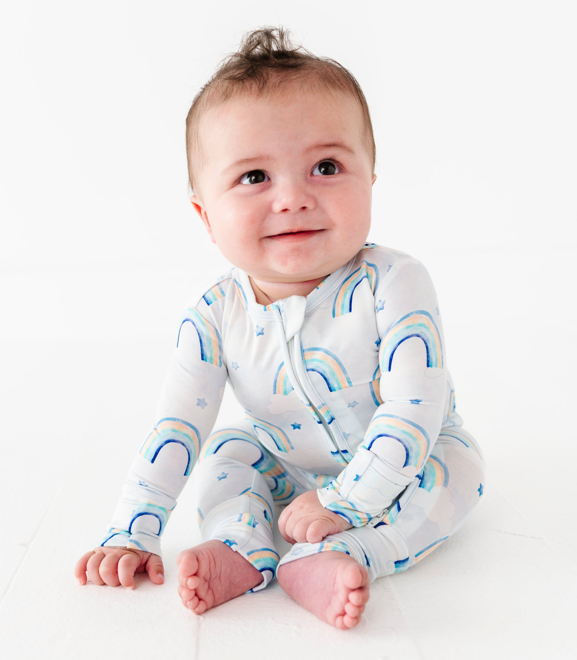 Baby wearing a bamboo convertible romper with blue watercolor rainbow patterns on a white background