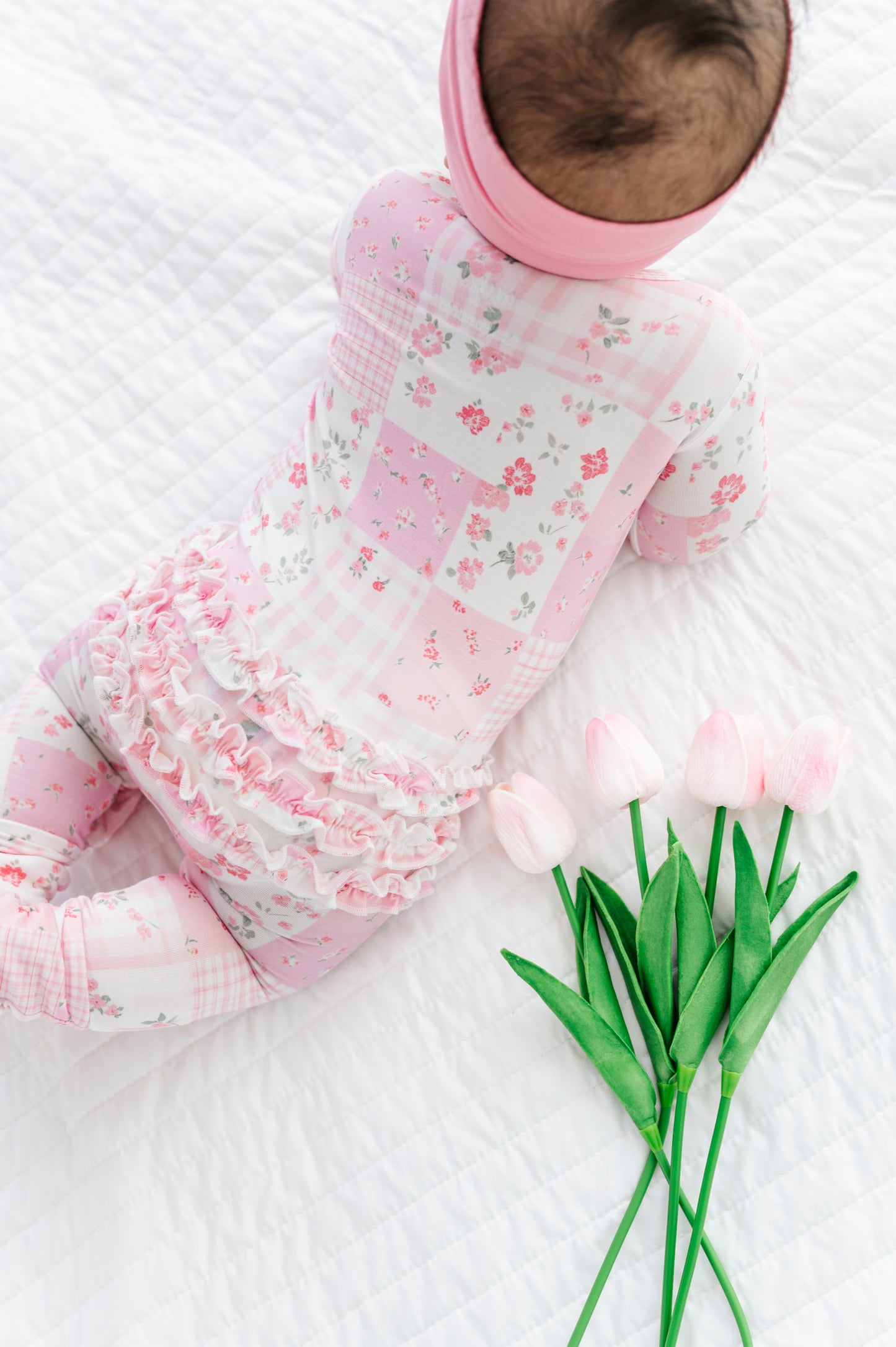 Baby wearing a pink floral bamboo zip romper with tulips on a white background
