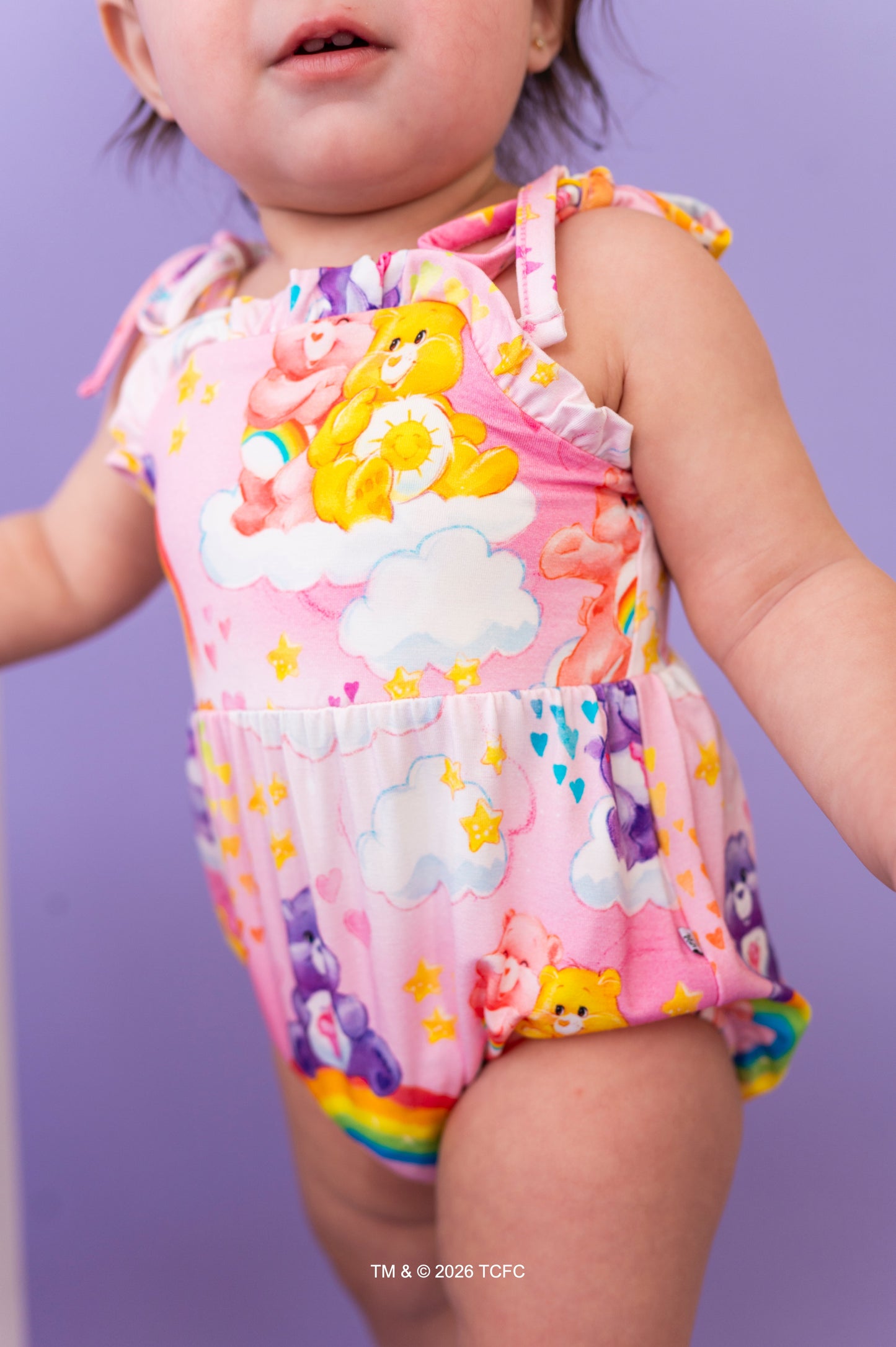 Child wearing a colorful Care Bears™ romper on a purple background