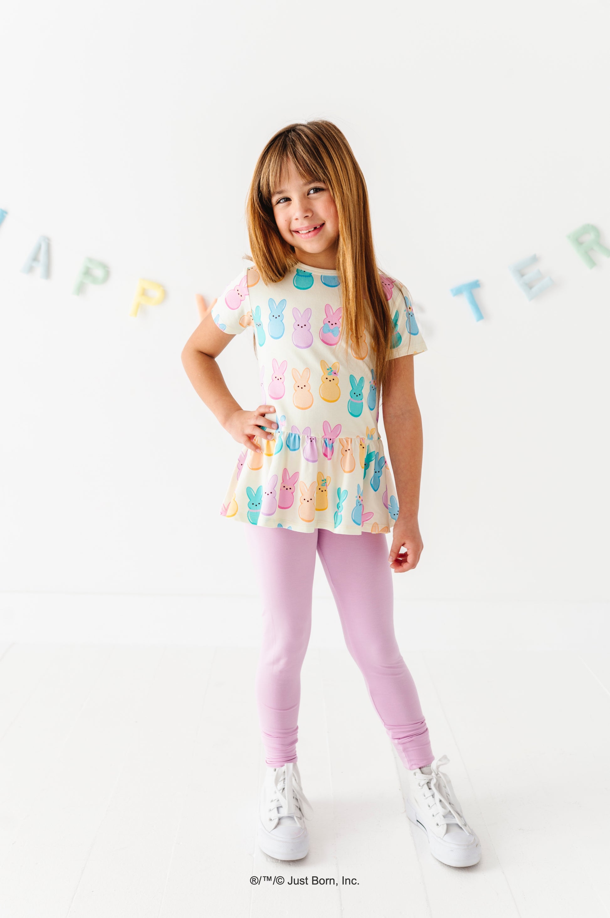 Young girl wearing a colorful PEEPS® peplum top and lavender leggings on a white background