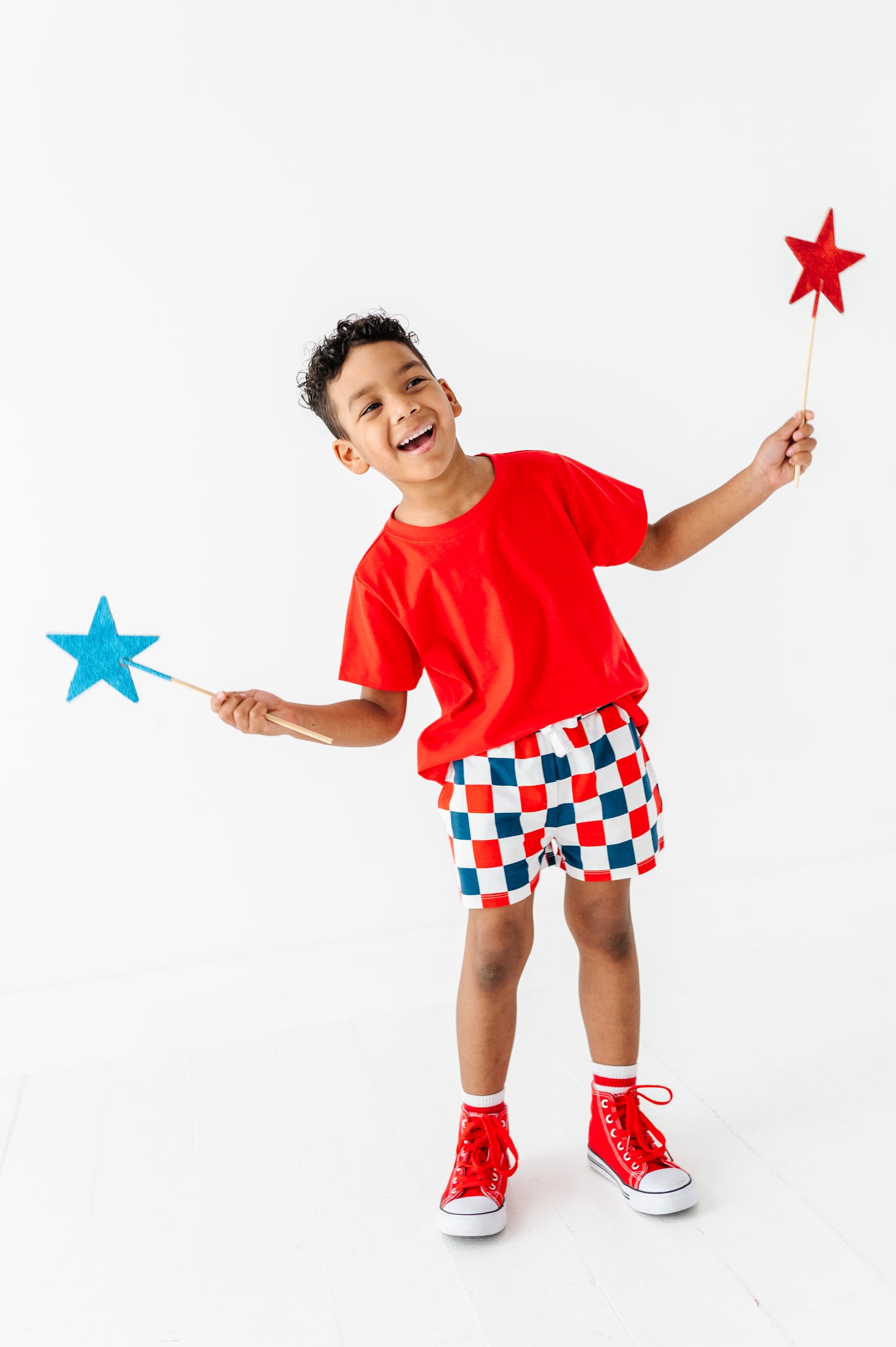Child in red shirt and checkered shorts holding star-shaped wands on a white background