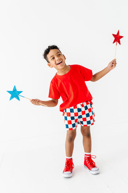 Child in red shirt and checkered shorts holding star-shaped wands on a white background
