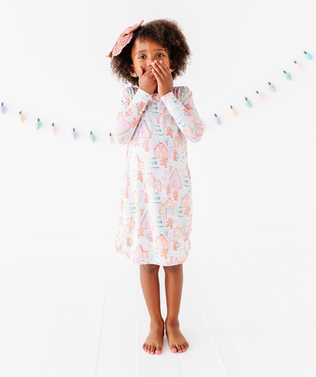 A little girl standing in a bright white room wearing a Christmas gingerbread-themed bamboo gown 