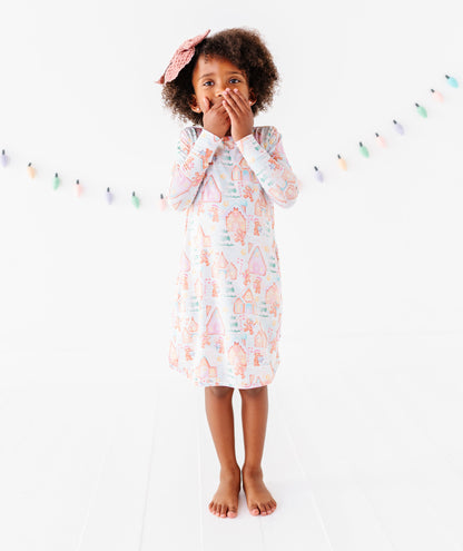 A little girl standing in a bright white room wearing a Christmas gingerbread-themed bamboo gown 