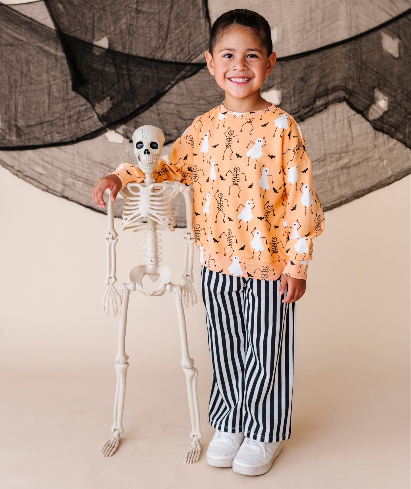 Child in Halloween-themed outfit with skeleton and black netting in the background