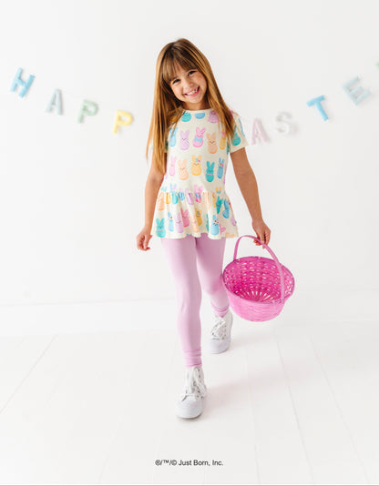 Young girl in a pastel PEEPS® Easter top holding a pink basket with 'Happy Easter' decorations in the background.