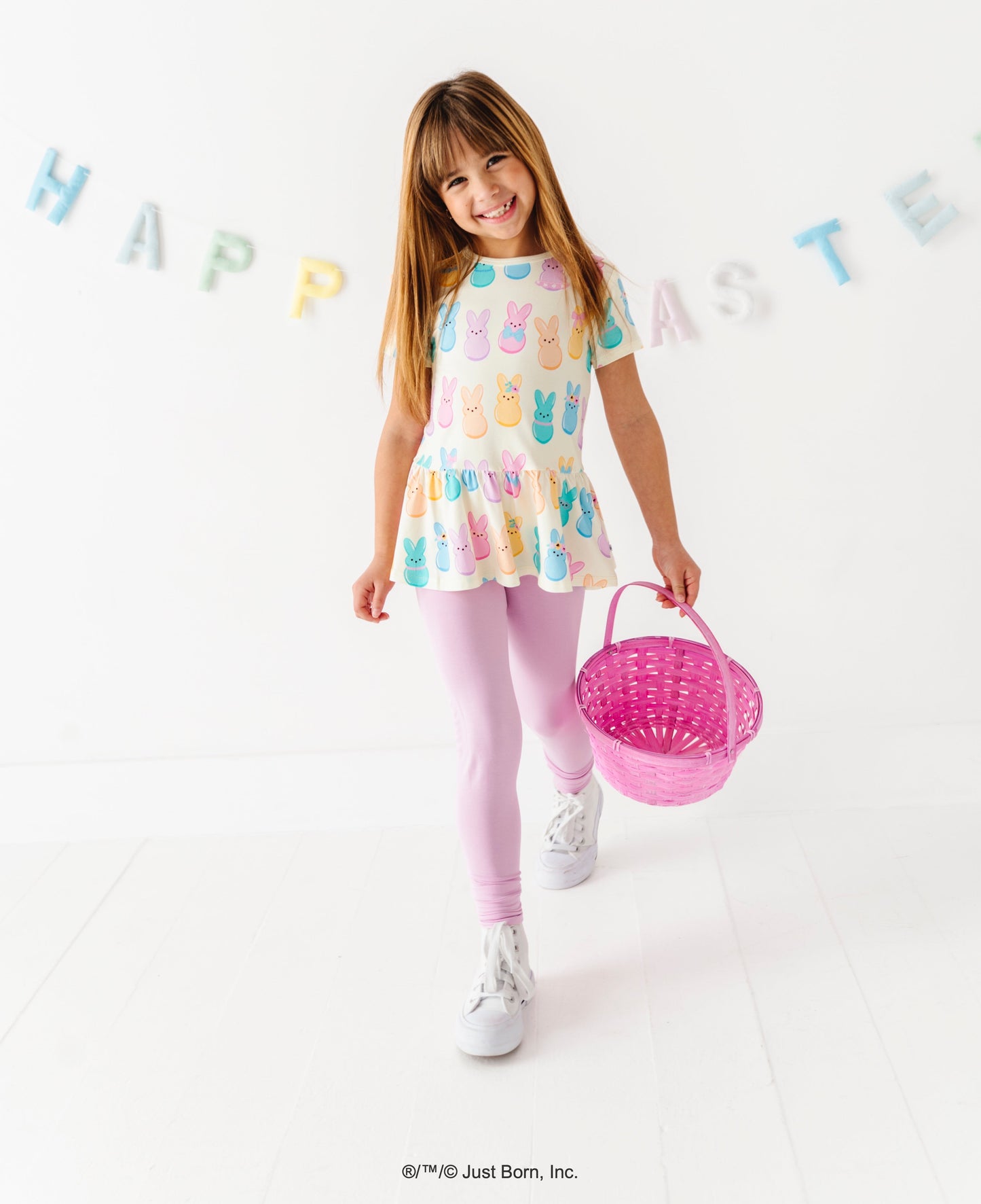 Young girl in a pastel Easter PEEPS®  top holding a pink basket with 'Happy Easter' decorations in the background.