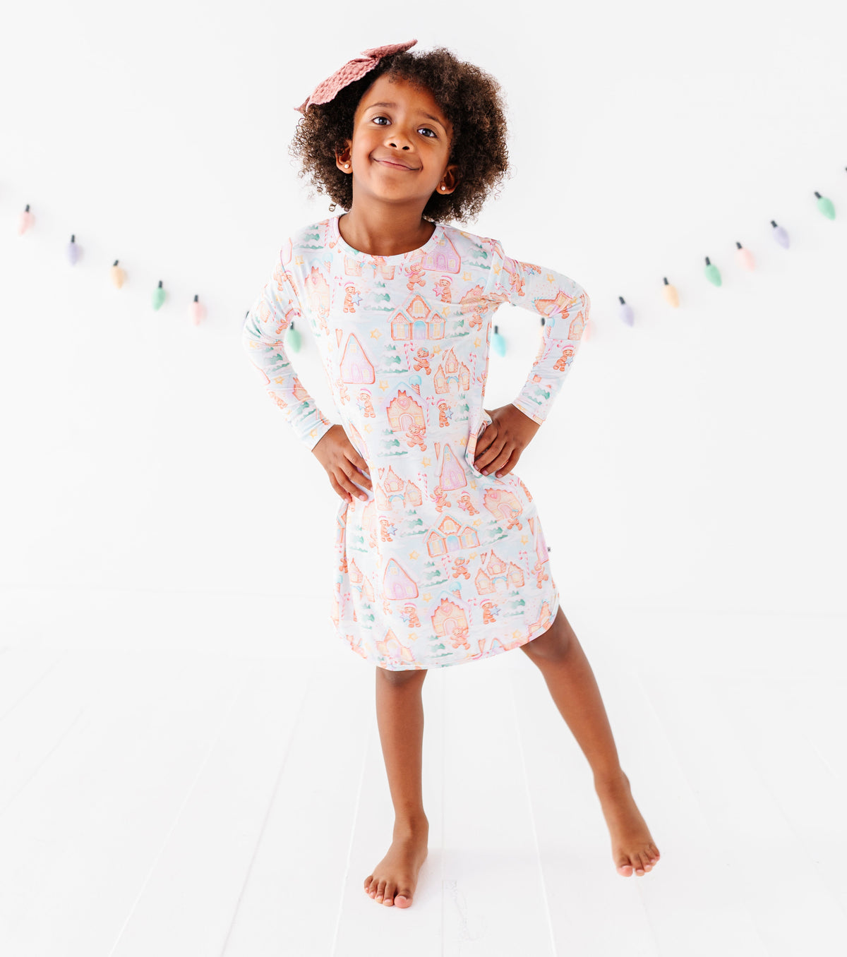 A little girl wearing a Christmas gingerbread-themed bamboo nightgown, standing in a bright white room 