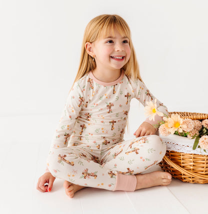 Child in bamboo Easter pajamas sitting next to a basket of flowers on a white floor.