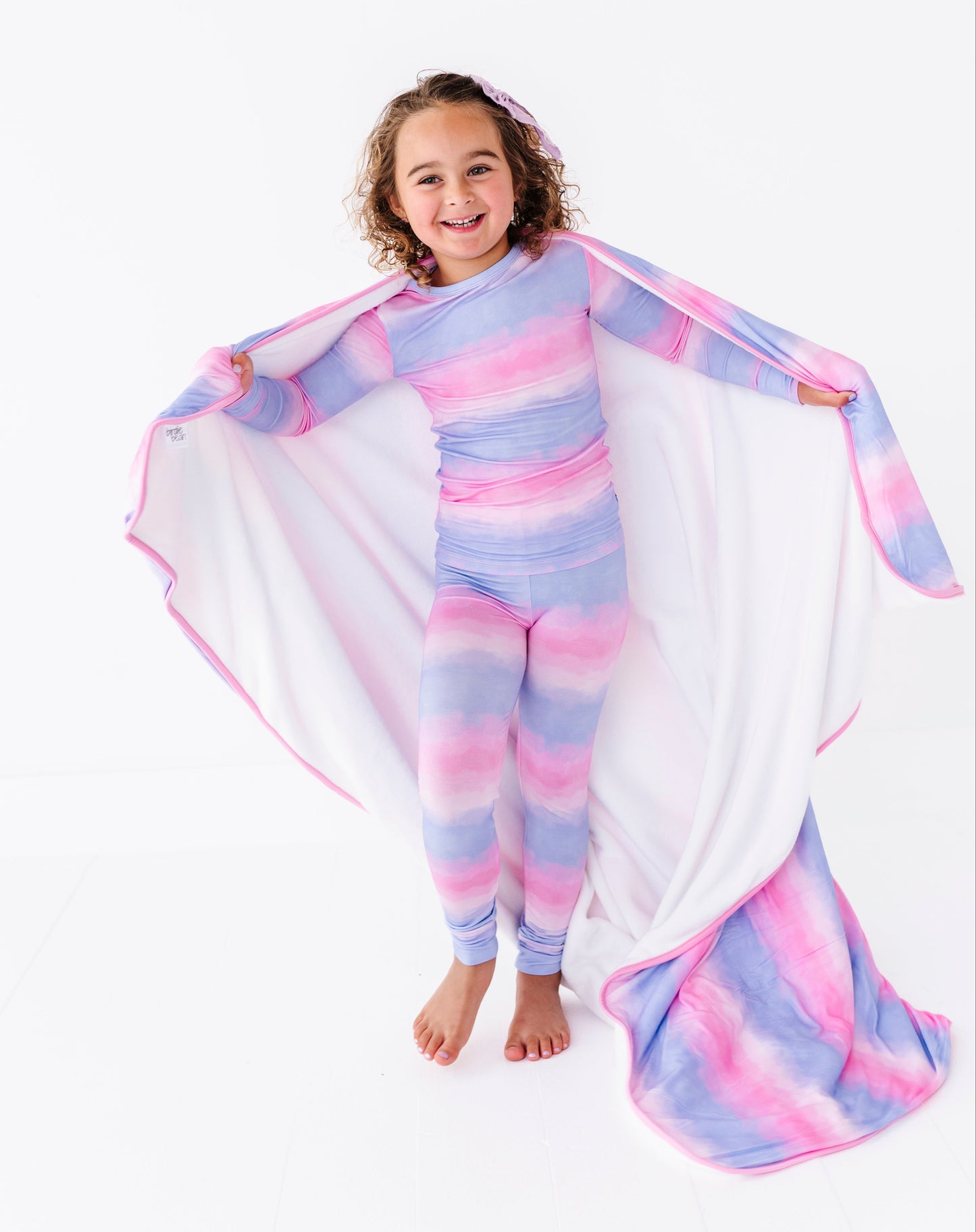 Child wearing a colorful striped bamboo pajama set with a matching bamboo blanket on a white background