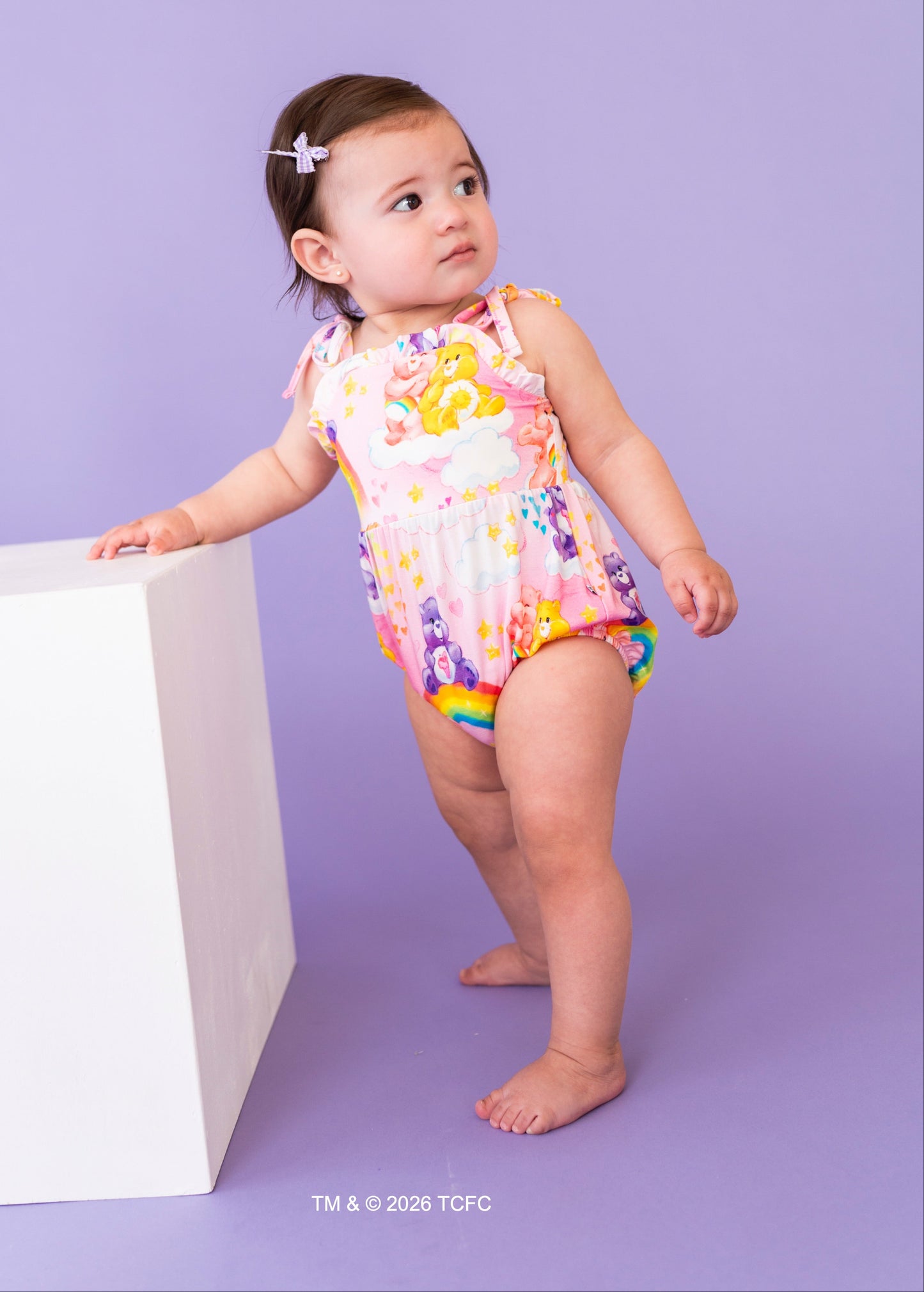 Child wearing a colorful Care Bears™ bubble romper on a purple background