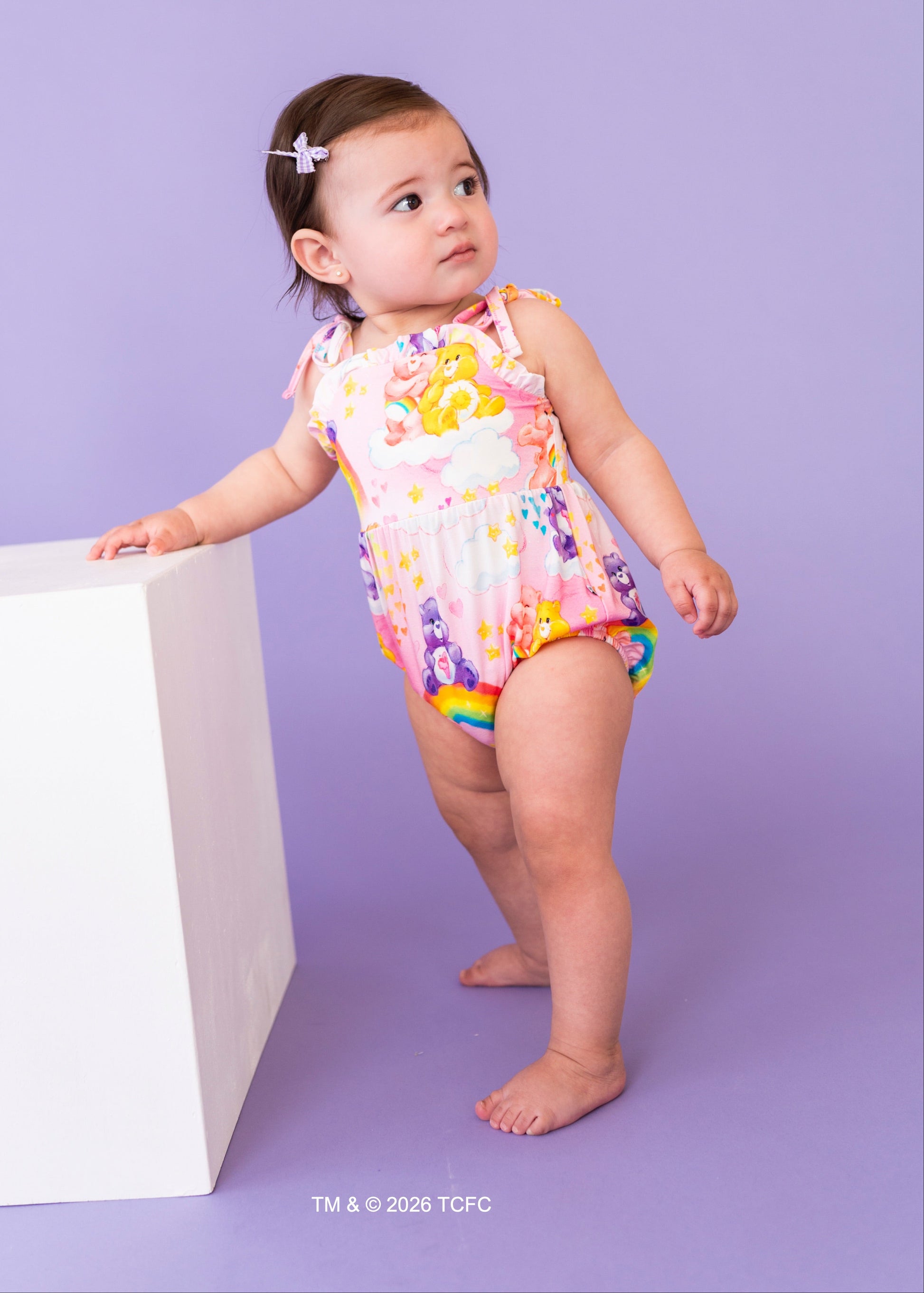 Child wearing a colorful Care Bears™ bubble romper on a purple background